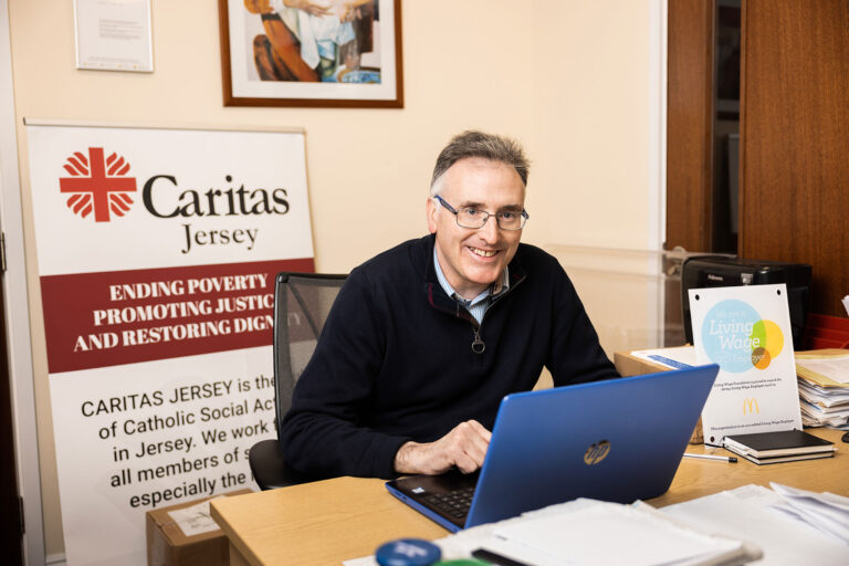 A man working at a desk with a laptop, and surrounded by office supplies.