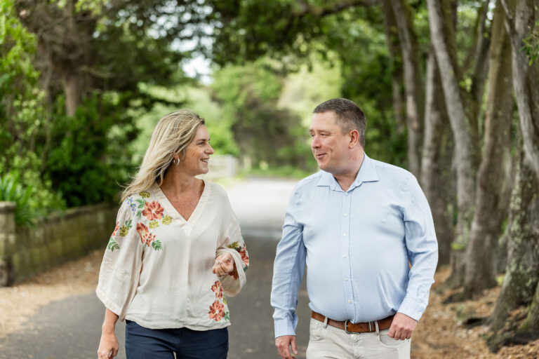 A man and woman stroll together along a scenic path surrounded by greenery.