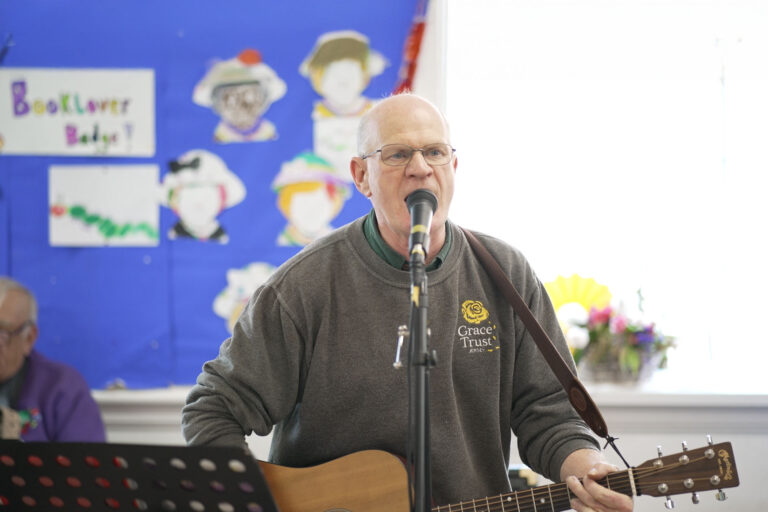 A man with glasses passionately singing into a microphone and playing the guitar.