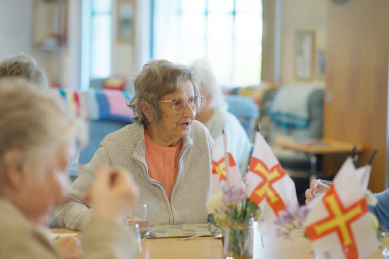 A woman seated at a table engaged in conversation with several other people around her.