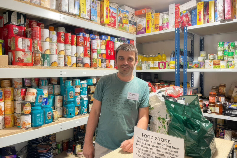 A man stands in front of shelves filled with various food items.