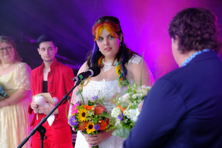 A bride stands in front of a microphone, smiling as she prepares to speak at her wedding ceremony.