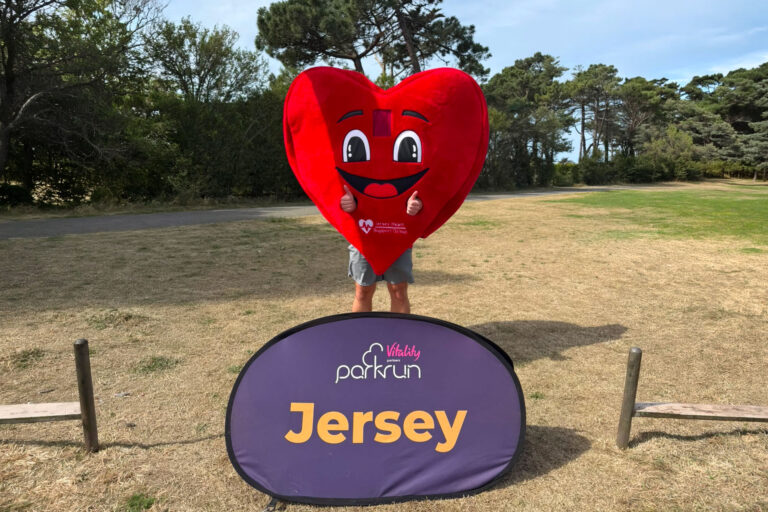 A person dressed in a heart-shaped costume standing in a sunny park, surrounded by greenery and trees.