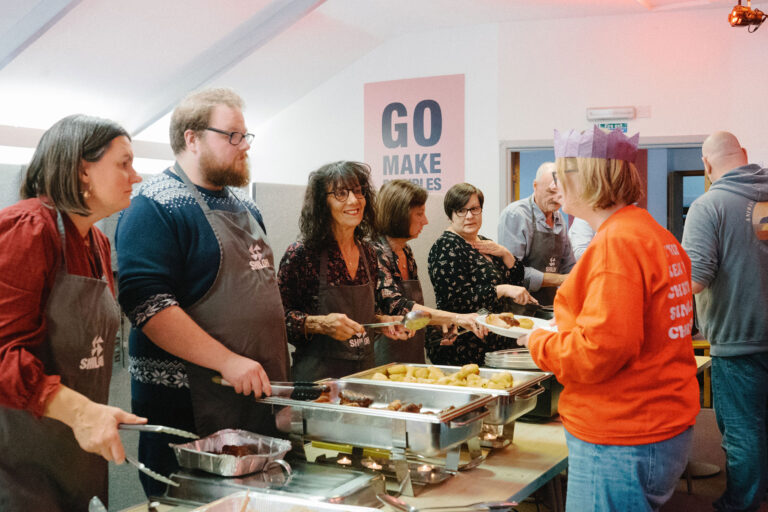 A group of people gathers around a buffet table filled with various dishes and food items.