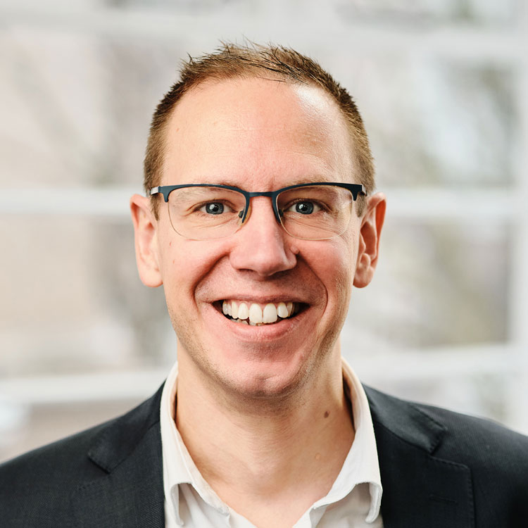 A man with glasses dressed in a suit smiles, exuding professionalism.